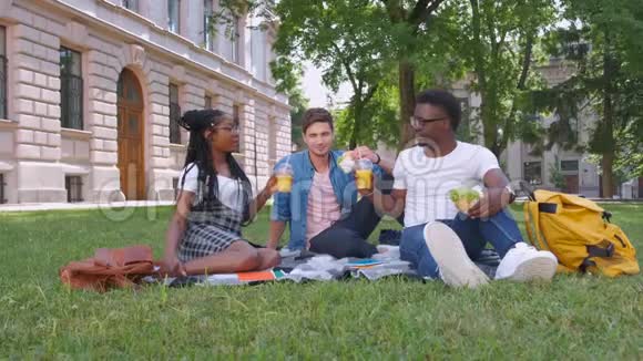 多种族的学生带着汉堡包在公园里放松视频的预览图