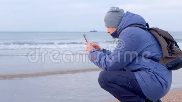 男子博主穿着冬天的衣服在海边拍视频的海浪打电话视频的预览图