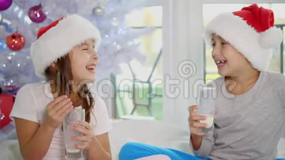 可爱的孩子戴着圣诞帽在家喝牛奶吃美味的饼干看起来非常满意视频的预览图
