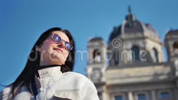 微笑迷人的旅游女孩摆在老式大教堂和蓝天背景低角度视频的预览图