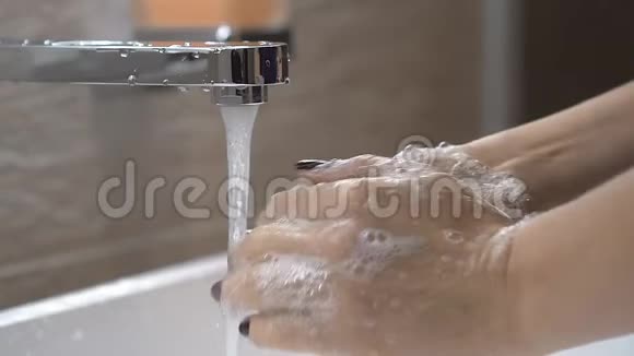 女人在浴室里用肥皂洗手从水龙头下的水流下把肥皂洗掉视频的预览图