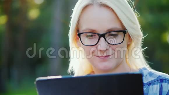 一位年轻女子戴着眼镜在公园里享受平板电脑的肖像美丽的阳光视频的预览图