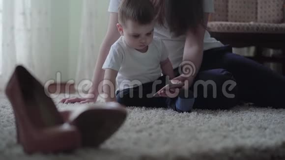 年轻女子和一个小男孩坐在地板上用手机给他看卡通片视频的预览图