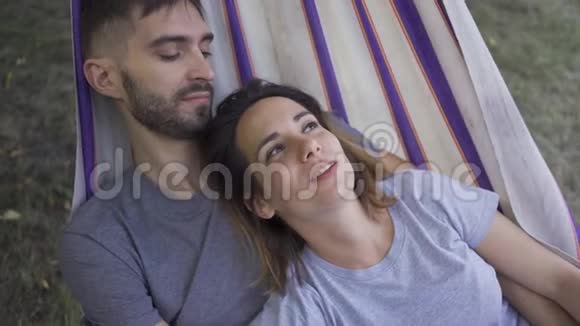 快乐的年轻白种人家庭躺在吊床在花园里一起放松爱的情侣一起在户外视频的预览图