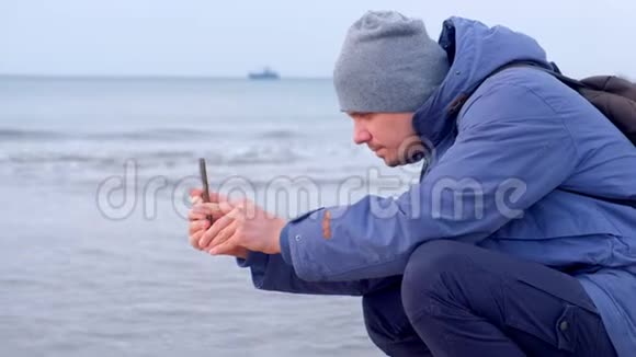 男子博主穿着冬天的衣服在海边拍视频的海浪打电话视频的预览图