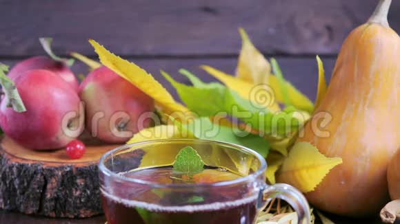 在收获南瓜苹果和五颜六色的秋叶的背景下木桌上放着热茶视频的预览图