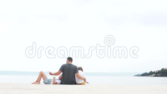 父亲和他的两个孩子一个男孩和一个女孩在白沙上放松后离开海滩暑假视频的预览图