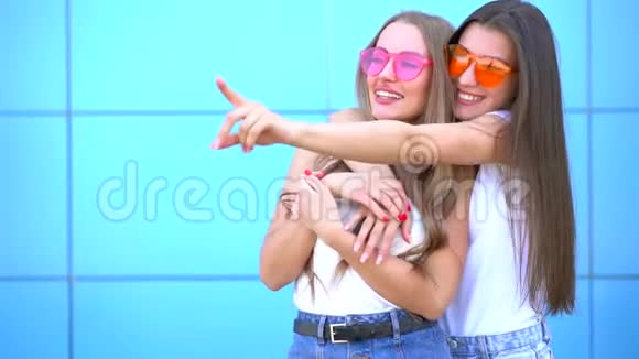 两个年轻的时髦女人在蓝墙上笑视频的预览图