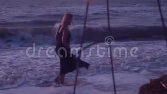 穿着黑色裙子的女人走在海滩上在海水里海浪里泡沫里穿过石头泥土泥土视频的预览图