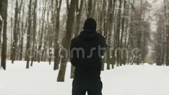 一个穿着黑色运动服的年轻人带着头罩在冬天白雪皑皑的城市里进行训练视频的预览图