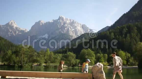 妈妈两个孩子和一只狗正在一座美丽的山的背景下在一个山湖的岸边休息视频的预览图