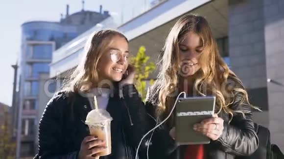 两位年轻的高加索妇女使用数码平板电脑在市中心散步时开心地微笑着的肖像视频的预览图