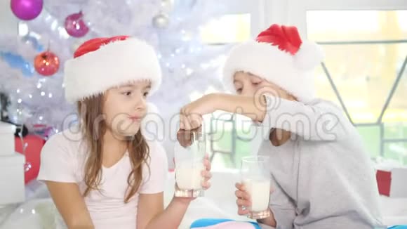 可爱的孩子戴着圣诞帽在家喝牛奶吃美味的饼干看起来非常满意视频的预览图