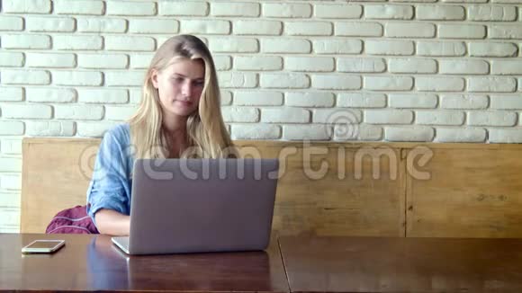 年轻漂亮的金发女人坐在咖啡馆里用她的笔记本电脑视频的预览图