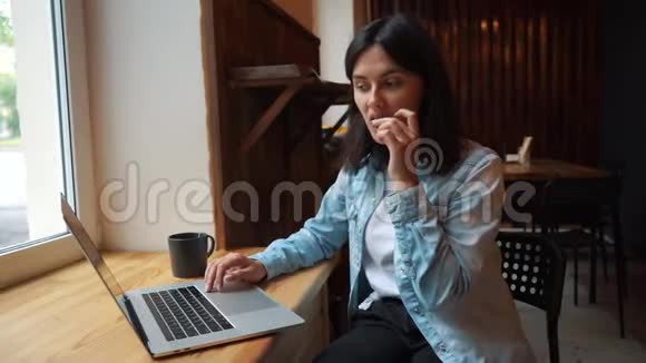 在笔记本电脑前的咖啡馆里吃巧克力的女孩视频的预览图