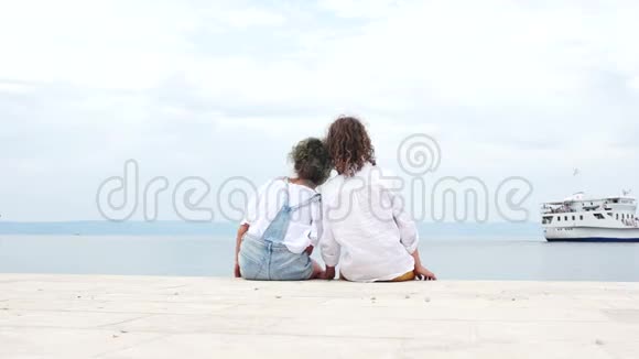 快乐的孩子们一个小男孩和一个女孩哥哥和姐姐坐在海边看着一艘帆船视频的预览图