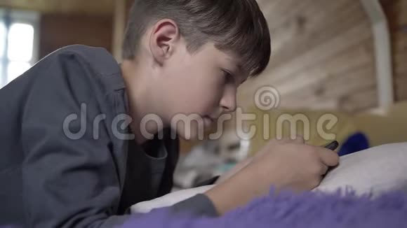 男孩躺在床上用电话青少年和朋友聊天玩游戏玩得开心视频的预览图