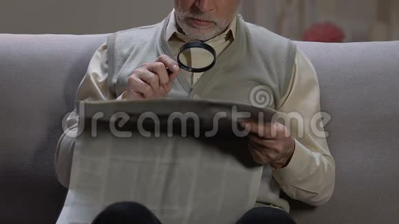 老人坐在沙发上用放大镜阅读报纸文章视频的预览图