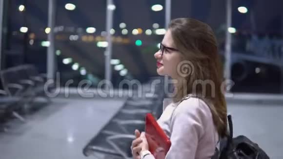 一个年轻美丽微笑的女孩手里拿着一台笔记本电脑和一个公文包沿着机场空无一人的候机楼走着视频的预览图