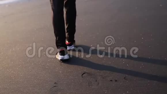 穿着时髦的运动鞋在黑色闪亮的沙滩上行走在沙滩上留下脚印视频的预览图