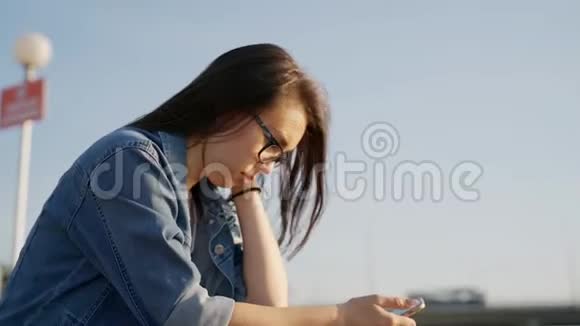 戴眼镜的女孩手里拿着手机坐在户外的台阶上慢动作视频的预览图