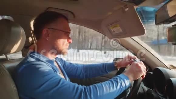 白色司机穿着蓝色衬衫驾驶汽车保护眼睛免受阳光与汽车遮阳延长冬天的午后视频的预览图