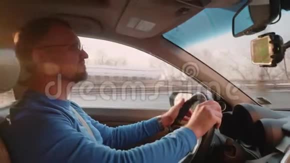 白色司机在有背光的车里司机在阳光下蹲着智能手机在手机保持架后视镜下视频的预览图