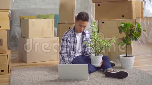 年轻的亚洲男人搬到一个新公寓坐在地上的笔记本电脑前视频的预览图