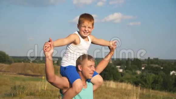 快乐的父亲抱着他微笑的儿子在阳光明媚的夏日在草地上旋转爸爸和他的红视频的预览图