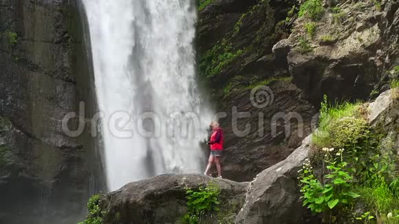 穿红色夹克衫的女人走在大瀑布附近视频的预览图