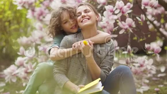可爱的小男孩和他的母亲在一棵盛开的木兰树上家庭幸福母亲节视频的预览图