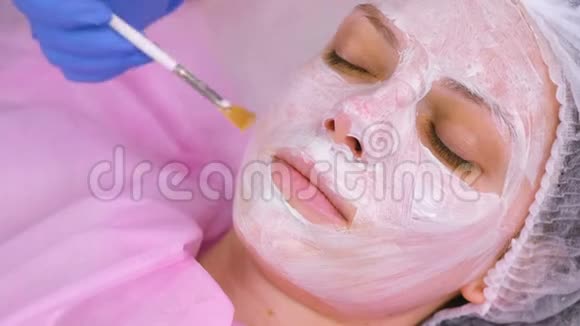 美容师用刷子把面具戴在女人脸上滋润的脸面的特写视频的预览图