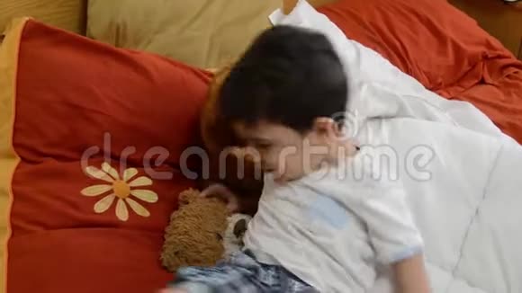 可爱的两岁男孩把泰迪熊放在父母的床上睡觉视频的预览图