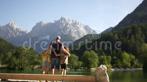 家人欣赏美丽的自然景观一位父亲和他的两个十几岁的孩子坐在岸边的长凳上视频的预览图
