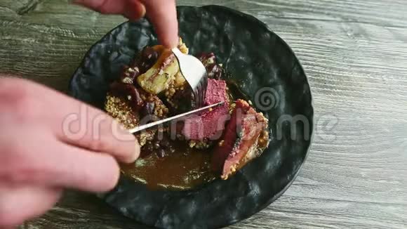 人手用叉子刀在黑盘上切半生肉牛排视频的预览图