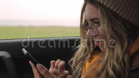 快乐的年轻女子在她的智能手机上在红灯时停车的座位上慢动作视频的预览图