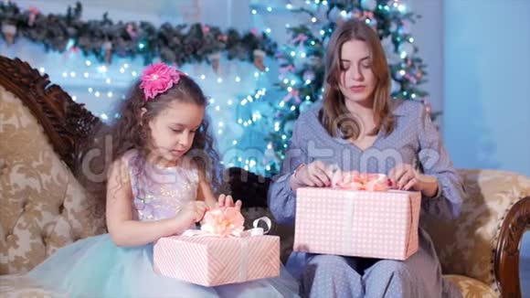 年轻快乐的母亲和她可爱的小女儿打开礼物看着内在在背景中快乐视频的预览图
