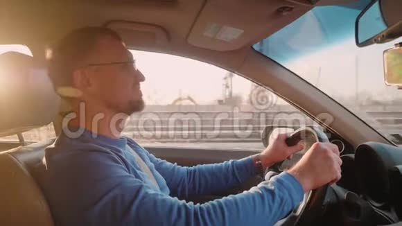 白色司机穿着蓝色长袖驾驶汽车转向相机微笑和挥手左手不错的背光视频的预览图