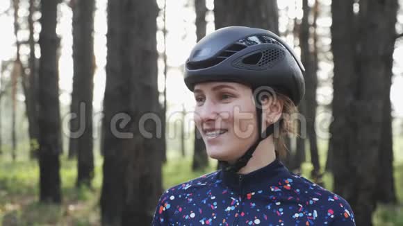 年轻迷人的女孩戴着黑色头盔和蓝色球衣骑自行车前戴上眼镜的肖像自行车概念慢节奏视频的预览图