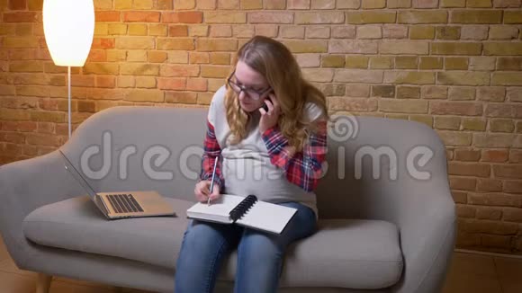 年轻怀孕女性的特写镜头使用笔记本电脑坐在电话里边说边做笔记视频的预览图