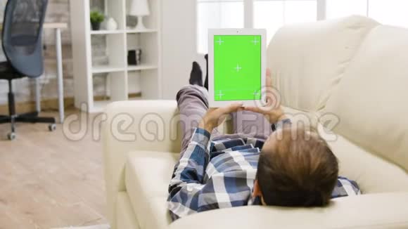 一位年轻男子在灯光明亮的客厅里手里拿着一台带有绿色屏幕的数字平板电脑视频的预览图