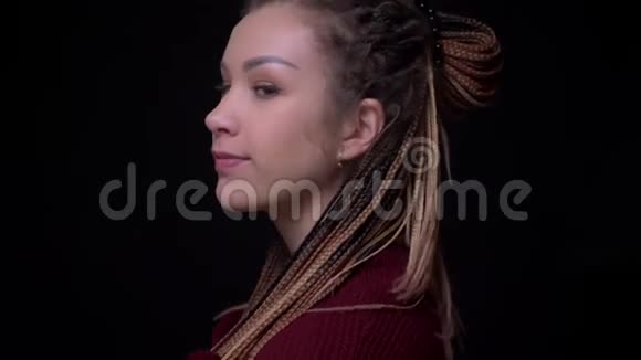 年轻的黑发女孩穿着刺和可怕的转向相机和微笑谦虚地害羞的黑色背景视频的预览图