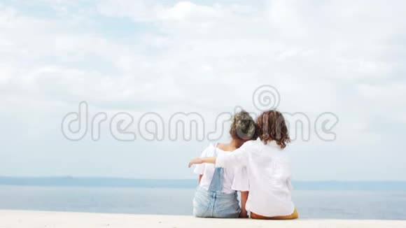 快乐的孩子们一个男孩和一个女孩坐在海边拥抱看着远处暑假旅行视频的预览图