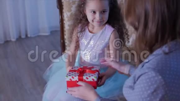 年轻快乐的母亲和她可爱的小女儿打开礼物看着内在在背景中快乐视频的预览图