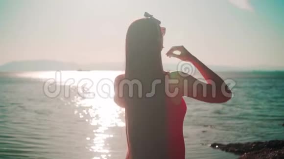 一个漂亮的女孩穿着红色的一件泳衣和眼镜站在海滨那个女孩摸了摸她的头发视频的预览图