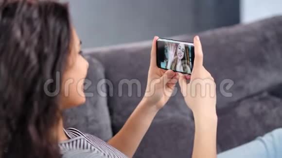 微笑的年轻女子在视频聊天连接上与女友使用智能手机特写视频的预览图