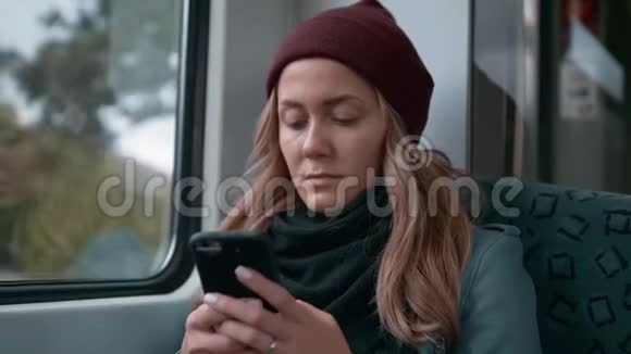 年轻的白种人女孩戴着红帽子乘坐地铁或电车使用电话打印信息慢动作视频的预览图