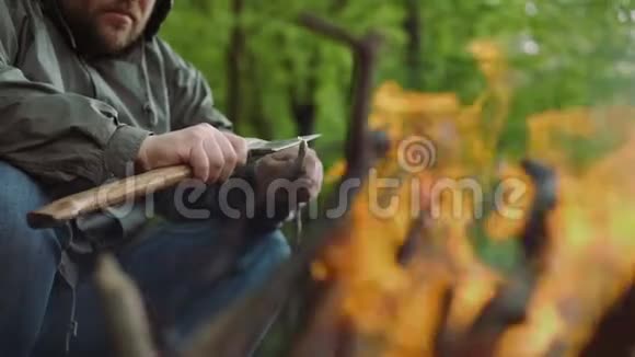 在野生落叶林的营地中在温暖的篝火附近用斧子和木头进行休闲壮汉的缓慢运动视频的预览图