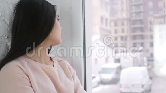 年轻的亚洲女人坐在窗前等着看时间视频的预览图