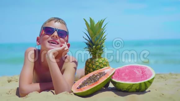 微笑的男孩躺在海岸上有一组异国情调的水果对抗大海视频的预览图